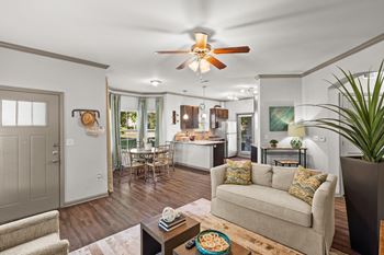 A living room with a ceiling fan, dining area with bay windows, hardwood floors, and crown molding.